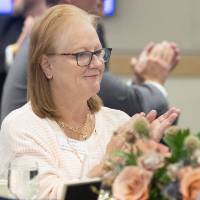Woman sitting at table, clapping while listening to speaker